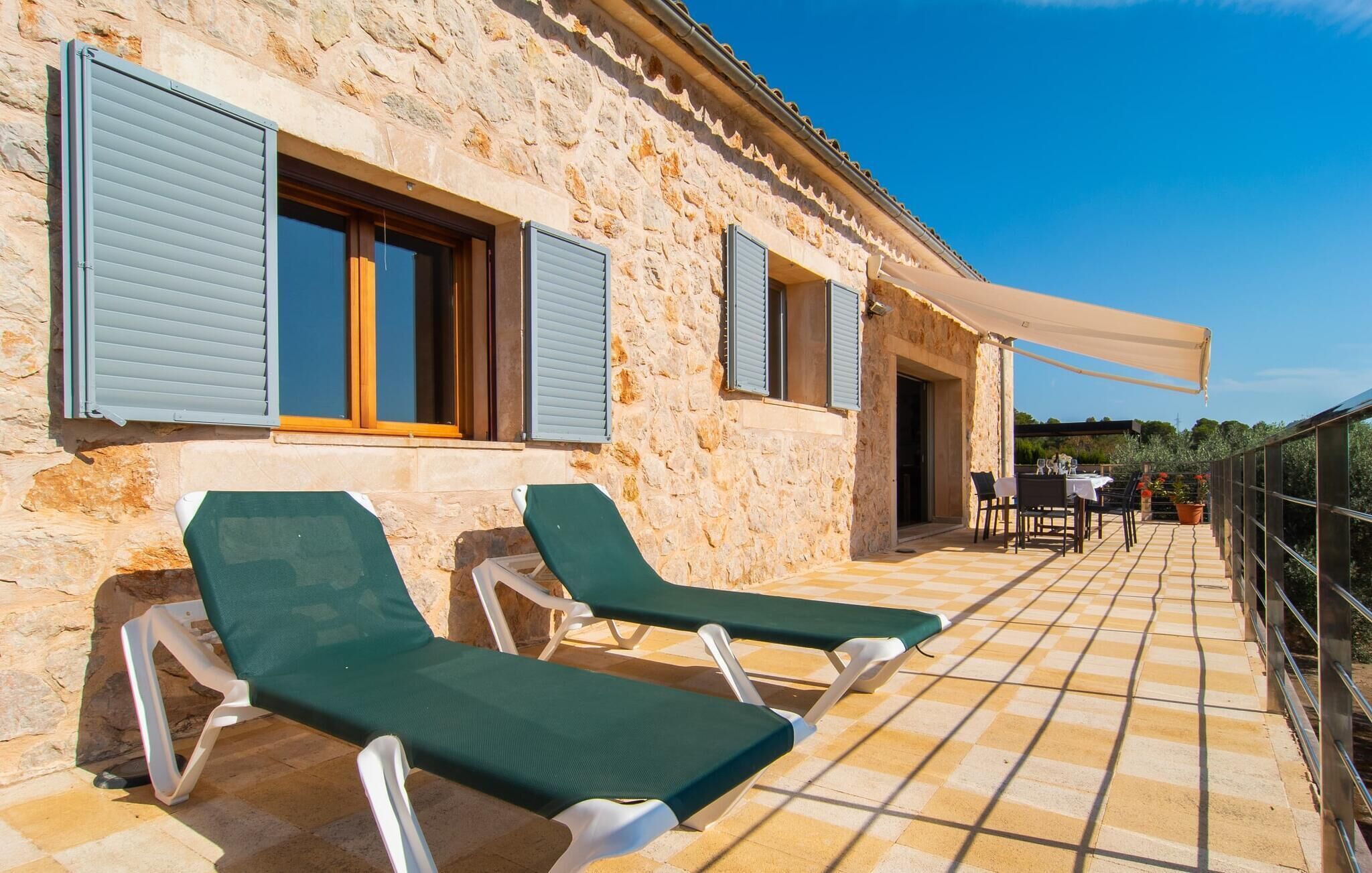 A stone building with two green lounge chairs on a tiled patio.