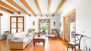 A spacious living room with a wooden ceiling, a sofa, a coffee table, and a chair. There is a door leading to a balcony with a view of greenery. - Beautiful home in Arta with private swimming pool, can be inside or outside (Arta)
