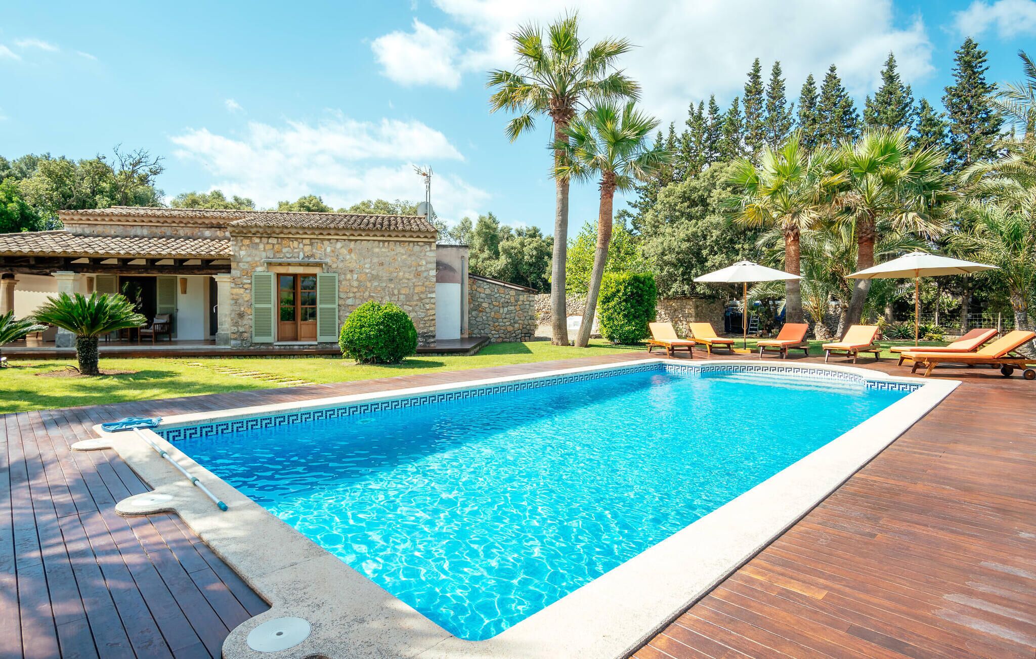 A swimming pool with a wooden deck, lounge chairs, and a stone building with shutters.
