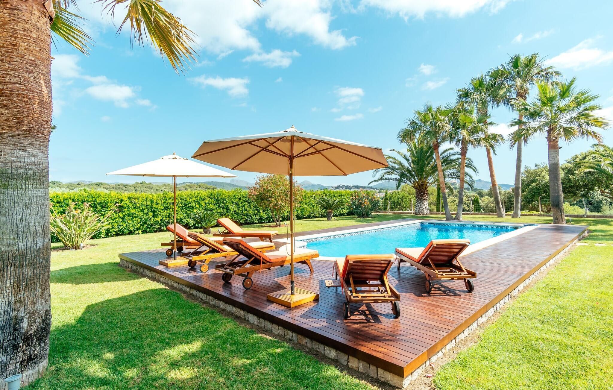 Zona de piscina con sillones de descanso y sombrillas, rodeada de palmeras y vistas al paisaje.