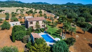 Una casa grande con piscina, rodeada de árboles y colinas.