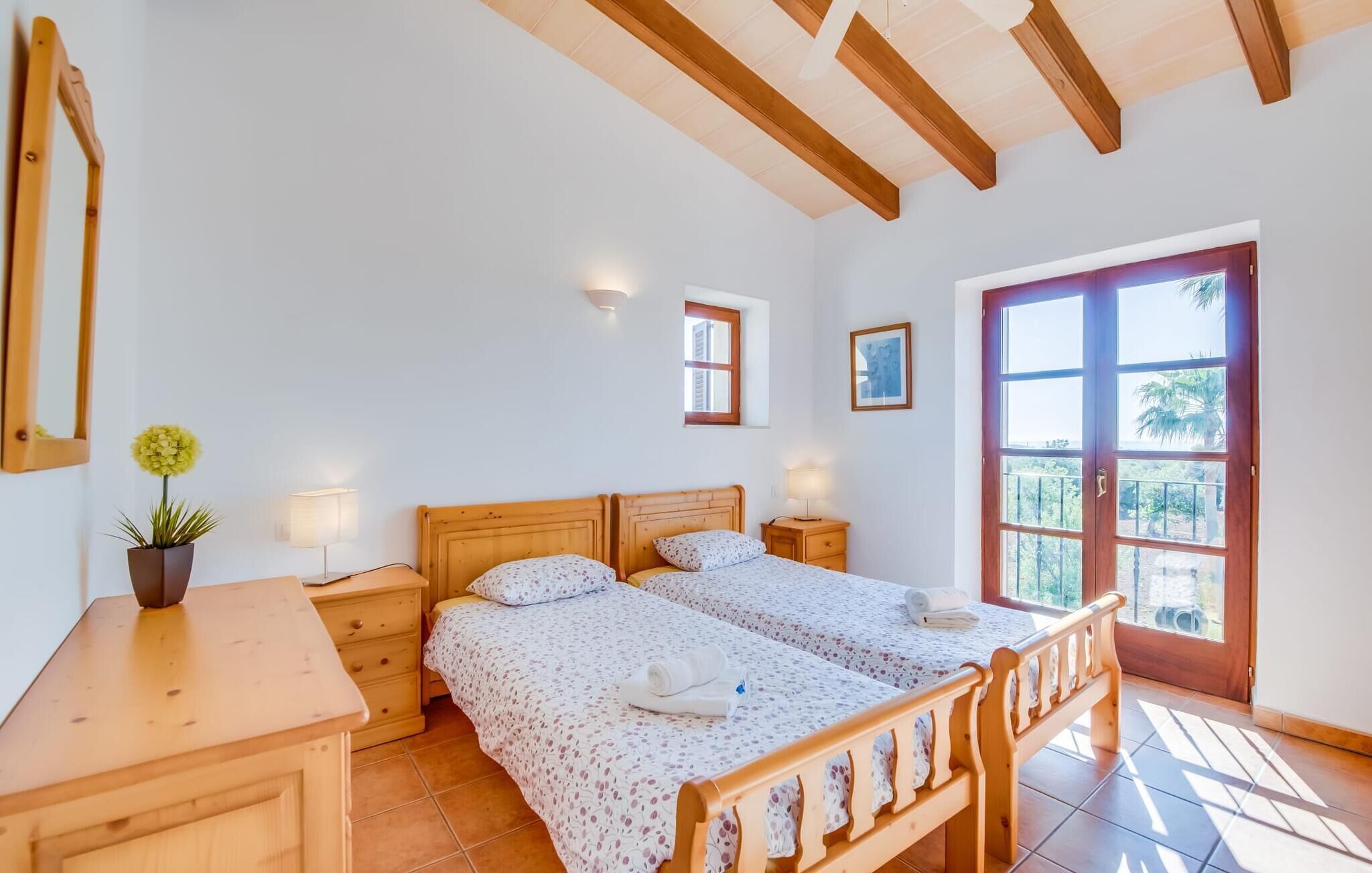 Un dormitorio con dos camas, un escritorio de madera, una planta en maceta, una ventana y una puerta que da al exterior.