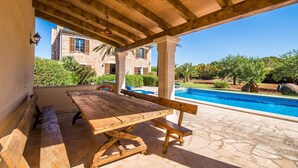 Un patio al aire libre con una mesa y bancos de madera, una piscina y un edificio de piedra al fondo.