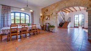 Un comedor amplio con un arco de piedra rústica, una mesa de madera con sillas y vistas al exterior a través de grandes ventanales.