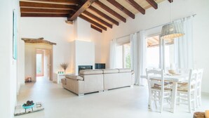 Ein großzügiger Wohnbereich mit Sofa, Esstisch, Stühlen, Kamin und einem großen Fenster mit Vorhängen.