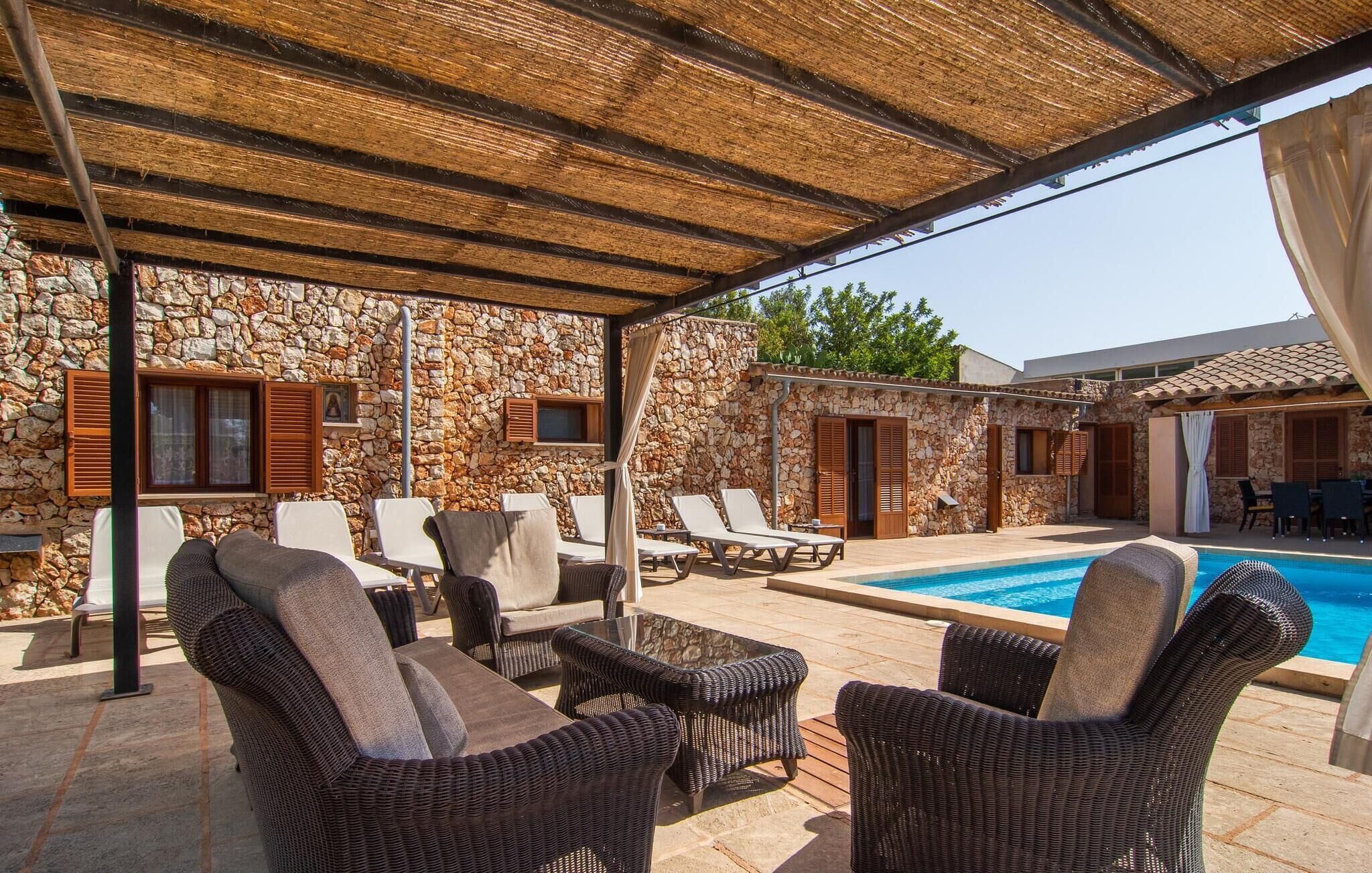 A covered outdoor area with stone walls, lounge chairs, and a pool.