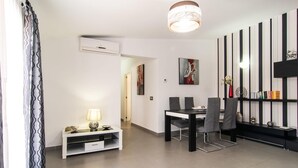 Uma sala de jantar moderna com uma mesa e cadeiras, um console branco com uma luminária, e um ar condicionado fixado na parede.