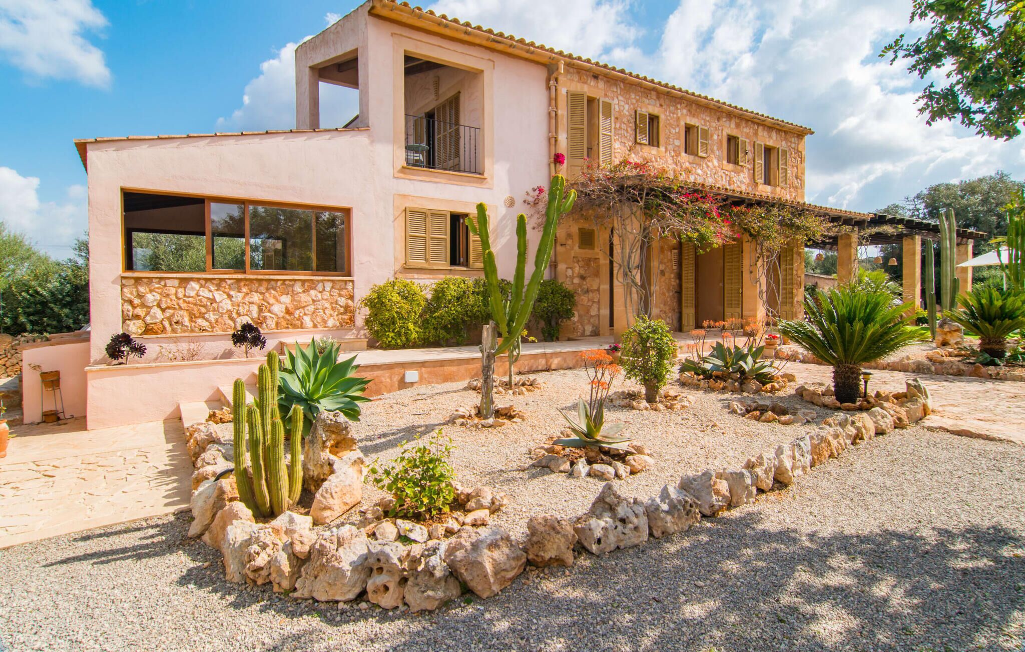 Ein zweistöckiges Haus mit einer Stein-Fassade, großen Fenstern und einem Garten mit Kakteen und anderen Wüstenpflanzen.