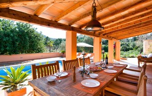 Un patio in legno con tavolo da biliardo adibito a zona pranzo, circondato da sedie e un tavolo imbandito con piatti e bicchieri.