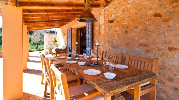 Un'area pranzo all'aperto con parete in pietra, tavolo e sedie in legno.