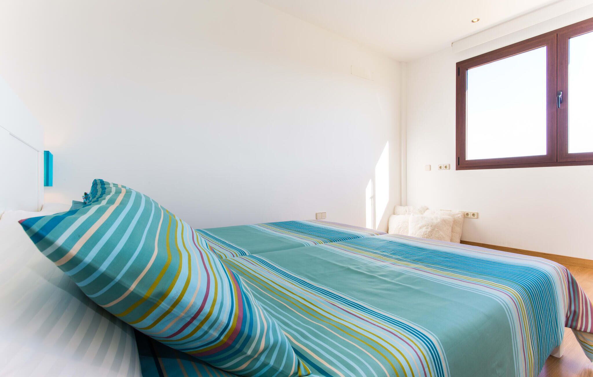 Un dormitorio con cama, ventana y lámpara fijada a la pared.