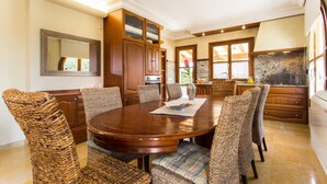 A dining area with a round wooden table, wicker chairs, and a kitchen in the background. - Cozy home in Manacor with private swimming pool, can be inside or outside (Manacor)