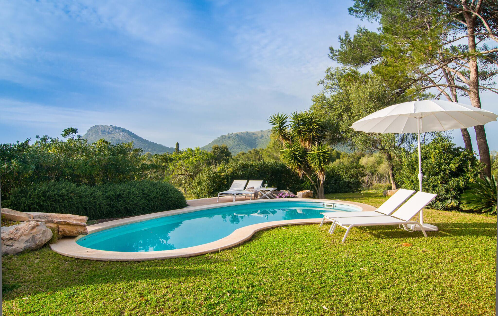 A swimming pool with two lounge chairs and an umbrella, surrounded by lush greenery and mountains in the background.