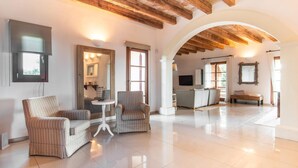 A spacious living area with a high ceiling, wooden beams, a tiled floor, and a cozy seating arrangement. - Amazing home in Cales de Mallorca (Cales de Mallorca)