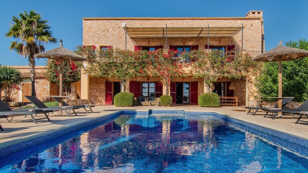 A poolside view of a stone building with a swimming pool, sun loungers, and a covered patio area. - Amazing home in Cales de Mallorca (Cales de Mallorca)