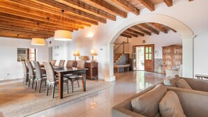 A spacious living area with a high wooden ceiling, a dining table with chairs, a sofa, and a staircase leading to another level. - Amazing home in Cales de Mallorca (Cales de Mallorca)
