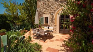 Un edificio de piedra con un patio que tiene una mesa y sillas, rodeado de plantas y flores.