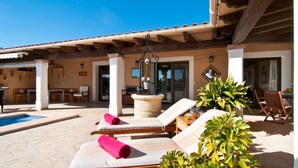 A sunlit outdoor lounge area with lounge chairs, a stone fountain, and potted plants. - Beautiful home in Portocolom (Portocolom)