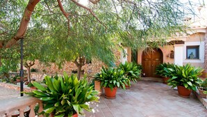 A courtyard with potted plants, a stone wall, and a wooden door. - Beautiful home in Portocolom (Portocolom)