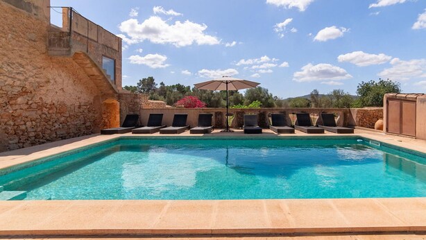A swimming pool with lounge chairs and an umbrella, surrounded by stone walls and vegetation. - Beautiful home in Cas Concos des Cavalle (Cas Concos des Cavalle)