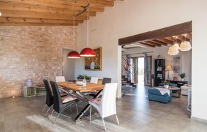 A spacious dining area with a wooden table and modern chairs, a brick wall, and a large window. - Lovely home in Ses Salines with private swimming pool, can be inside or outside (Ses Salines)