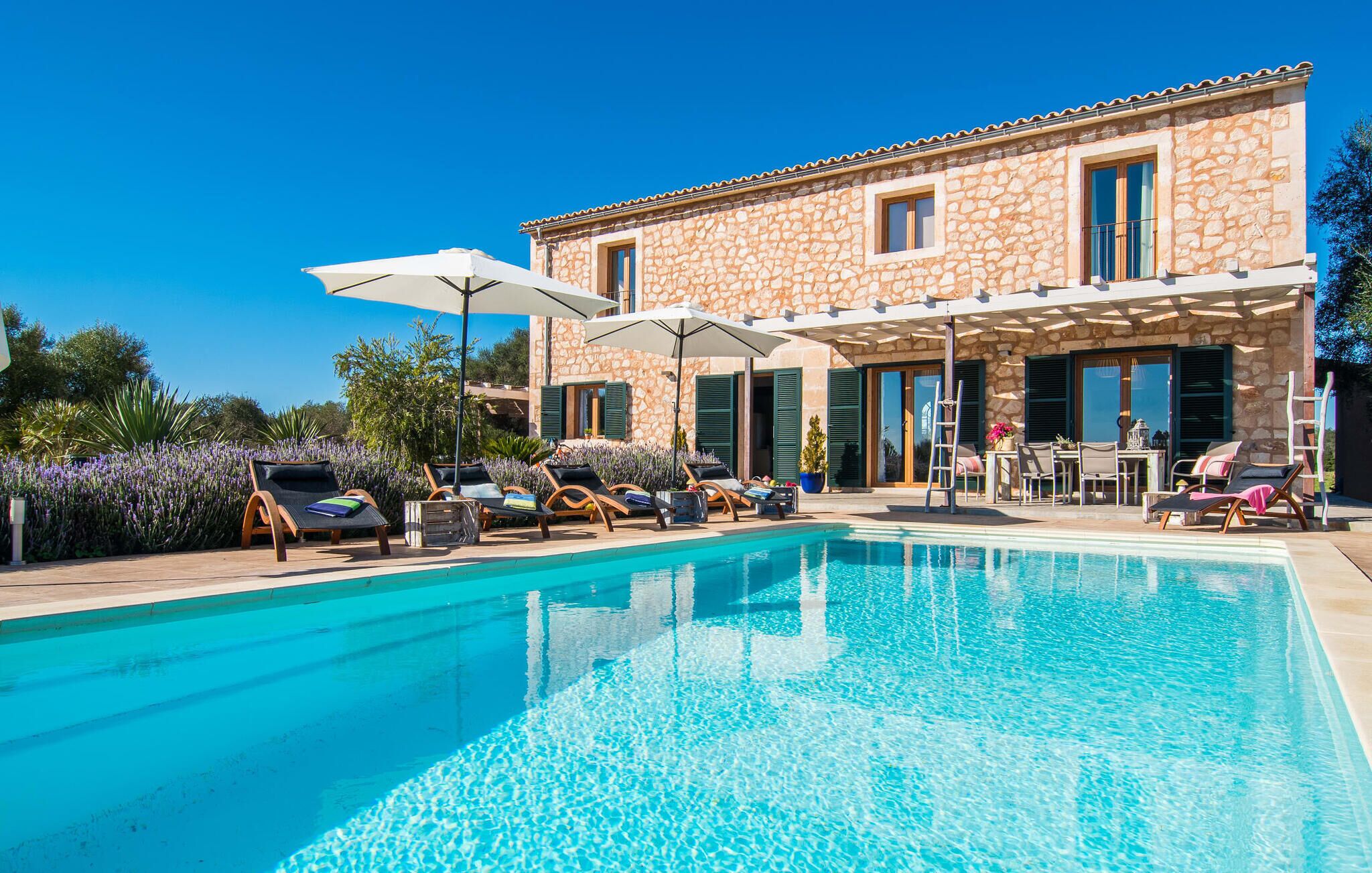 A poolside area with lounge chairs, umbrellas, and a stone building with large windows.