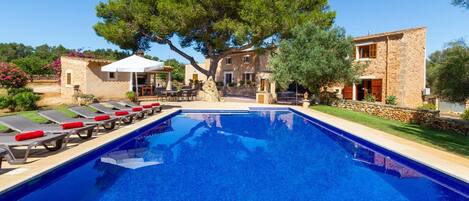 A swimming pool with lounge chairs, a stone building, and a large tree.