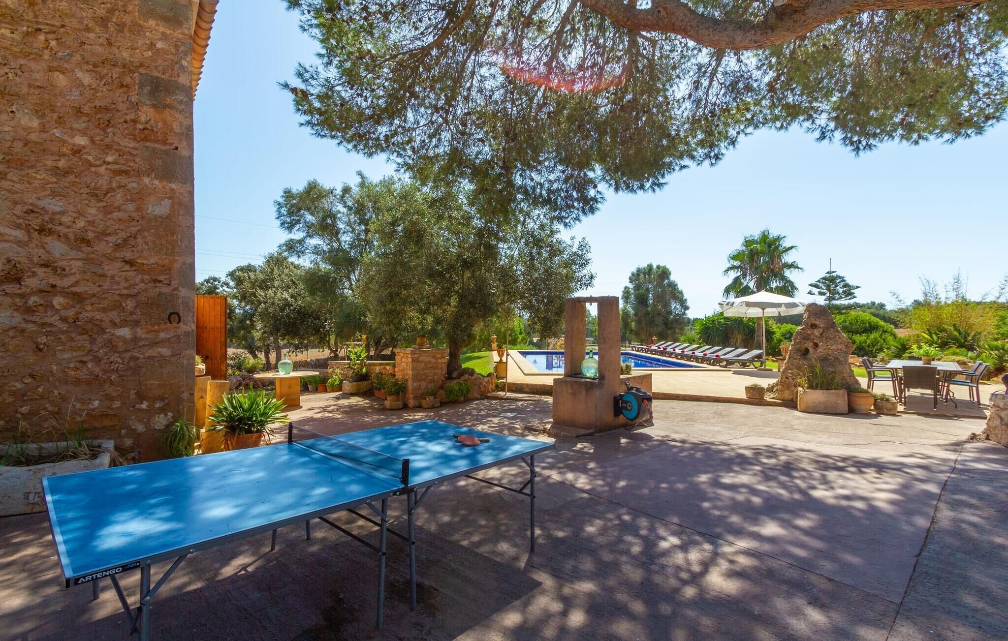 An outdoor pool area with a ping pong table, lounge chairs, and a stone structure.