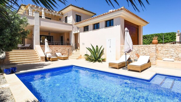 Une villa moderne dotée d’une piscine, d’un espace salon extérieur et d’un mur en pierre.