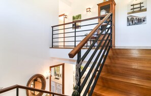 Eine Treppe mit Holzdielen und schwarzen Metallgeländern, die zu einer zweiten Etage mit einem Holzschrank und einem gerahmten Bild führt.