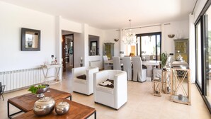 Un salon moderne avec un coin repas, une cuisine visible à travers une porte ouverte et une grande fenêtre qui laisse entrer la lumière naturelle.