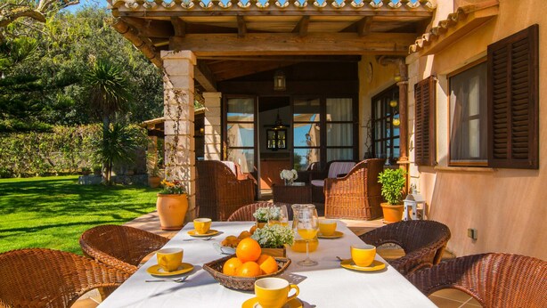An outdoor dining area with wicker furniture, a table set for breakfast, and a view of the garden. - Luxurious home in Arta with private swimming pool, can be inside or outside (Arta)