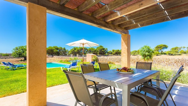 A covered patio with a table and chairs, overlooking a swimming pool and a stone wall. - Beach front home in Porto Cristo (Porto Cristo)