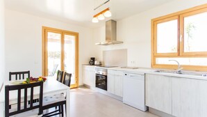 A modern kitchen with white cabinets, a built-in oven, a dishwasher, and a window with a wooden frame. - Beach front home in Porto Cristo (Porto Cristo)