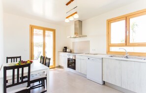 A modern kitchen with white cabinets, a built-in oven, a dishwasher, and a window with a wooden frame. - Beach front home in Porto Cristo (Porto Cristo)