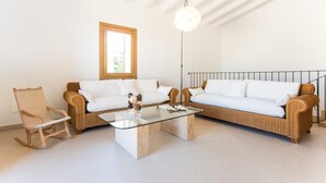 Een moderne woonkamer met twee witte banken, een glazen salontafel en een rieten fauteuil.