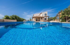 Una grande piscina con acqua cristallina, circondata da un edificio bianco con tetto in tegole e una pergola in legno.