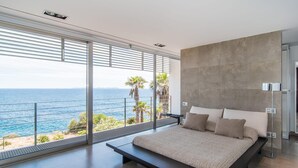 Une chambre moderne avec un grand lit, une vue sur la mer et un balcon agrémenté de palmiers.