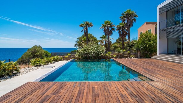 Une piscine dotée d’une terrasse en bois, entourée de palmiers et offrant une vue sur la mer.