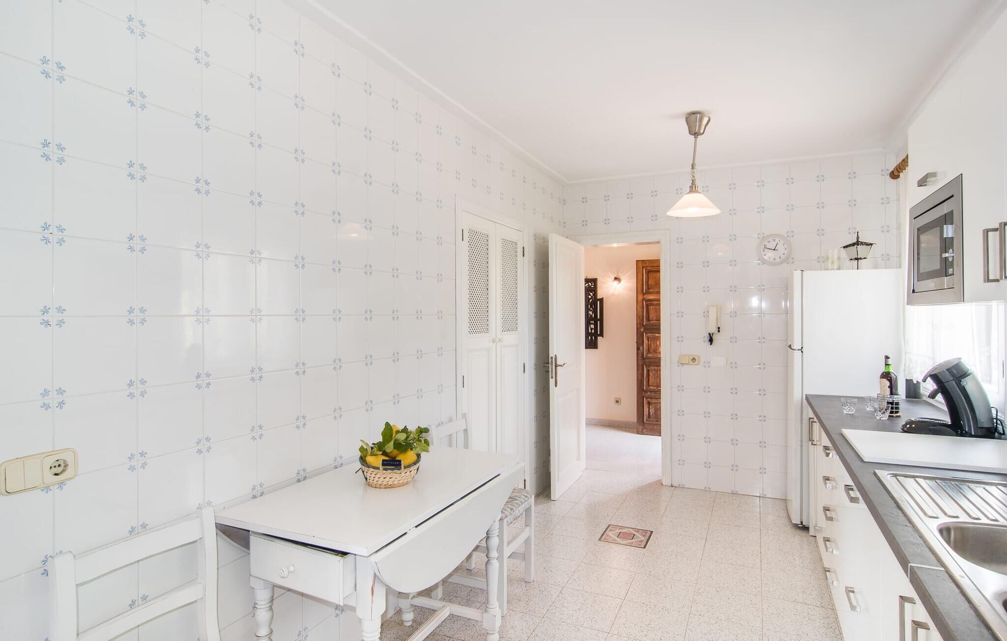 A kitchen with white tiled walls, a white countertop, and a hanging light fixture.