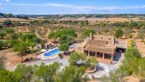 Eine Villa mit Schwimmbad, umgeben von Bäumen und offenen Feldern.