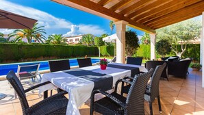 En udendørs terrasse med pool, overdækket siddeområde og udsigt til en boligbygning.