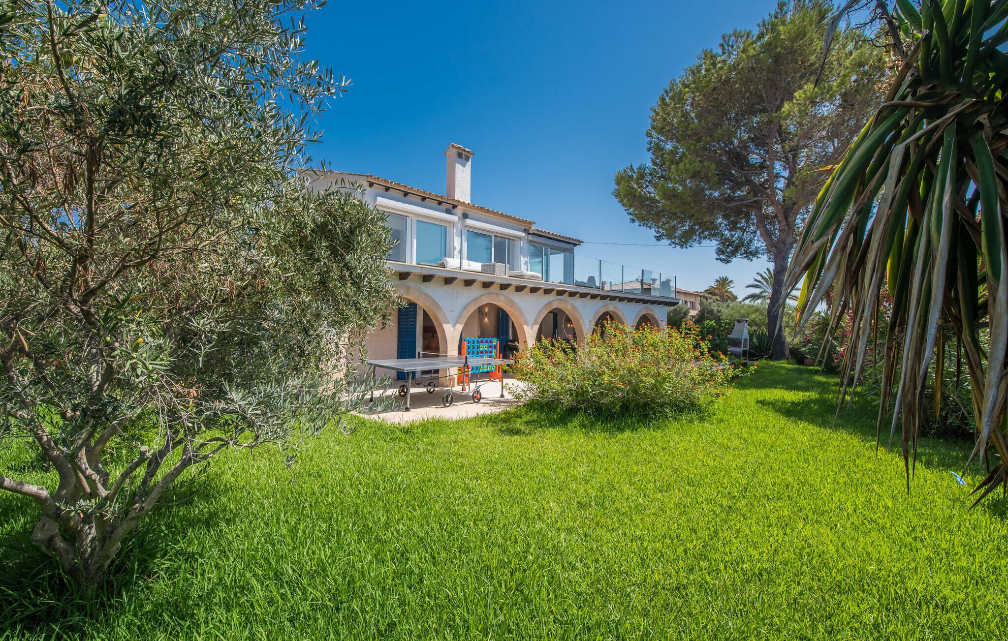 Una vila d'estil mediterrani amb un pati espaiós, finestres arquejades i vegetació exuberant.