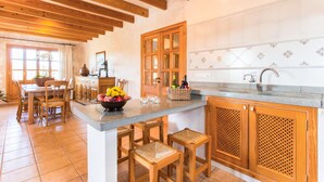 A kitchen with wooden beams, a central island with stools, a fruit bowl, and a tiled backsplash. - Luxurious home in Son Servera (Son Servera)