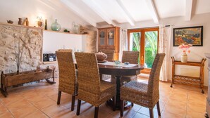 A dining area with a round table, wicker chairs, a stone wall, and a view of greenery through a glass door. - Awesome home in Arta with private swimming pool, can be inside or outside (Arta)