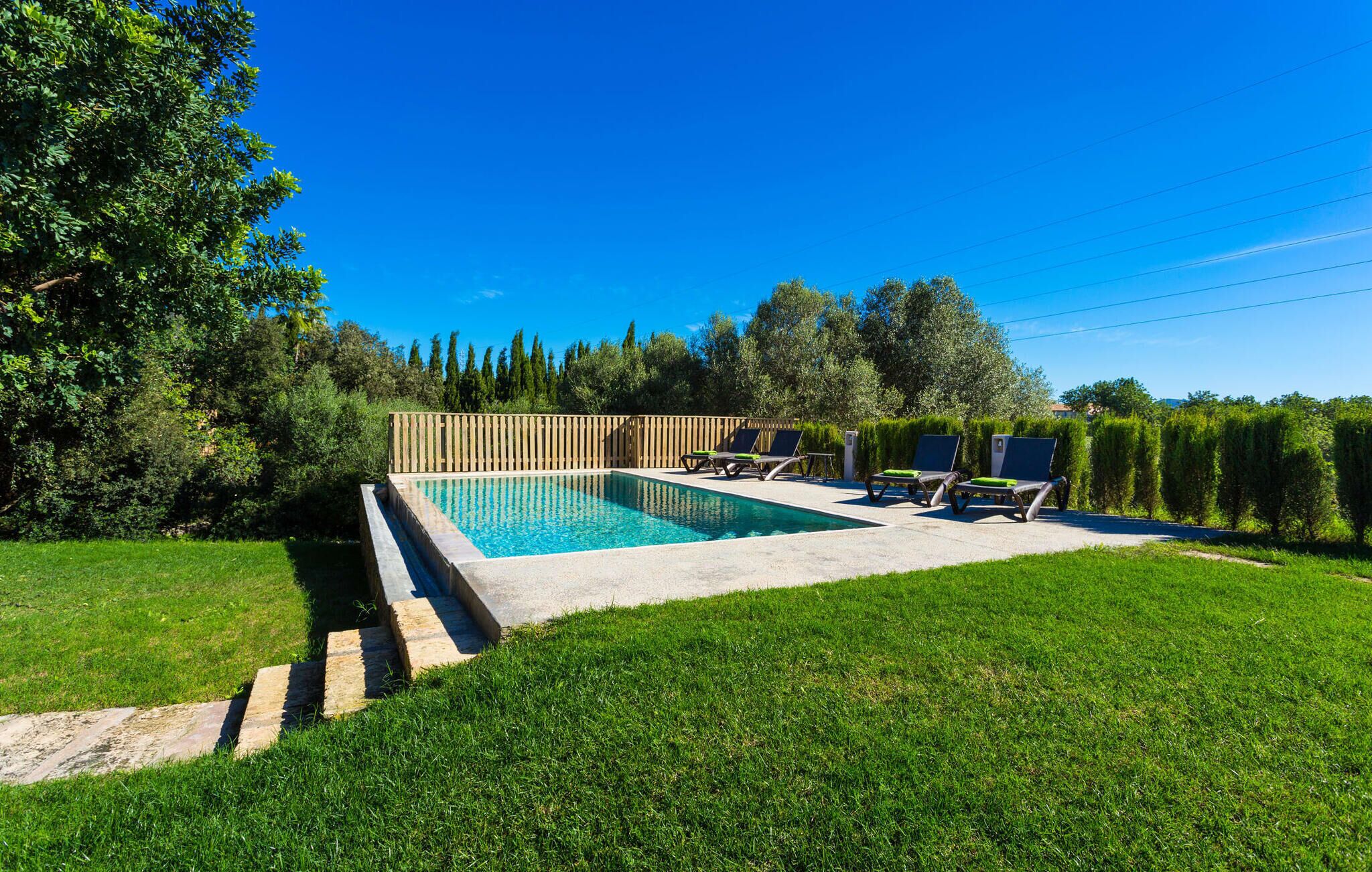 Une piscine rectangulaire dotée d’une terrasse en bois et de chaises longues.