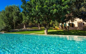 Piscina com água azul cristalina, rodeada por vegetação exuberante e um muro de pedra.