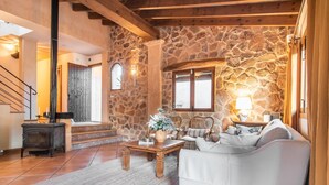 A cozy living room with a stone wall, a fireplace, a sofa, and a coffee table. - Awesome home in Capdepera with private swimming pool, can be inside or outside (Capdepera)