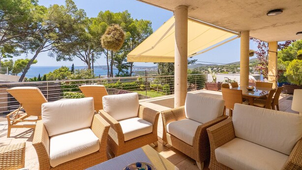 Un espace extérieur aménagé, abrité et doté de mobilier en osier, offrant une vue sur la mer.