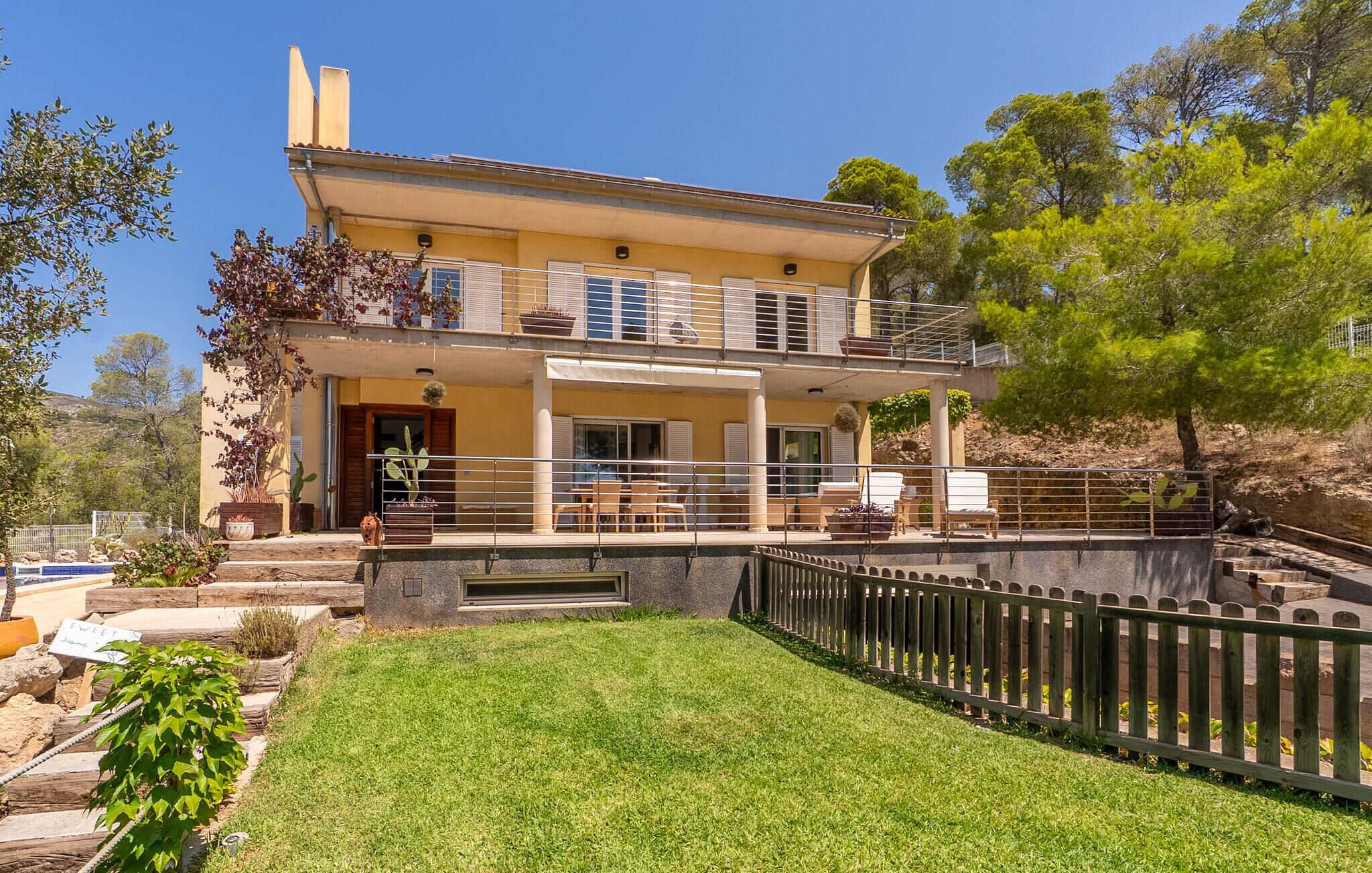 Ein zweistöckiges Haus mit Balkon, Schwimmbad und einem von einer Hecke umgebenen Garten.